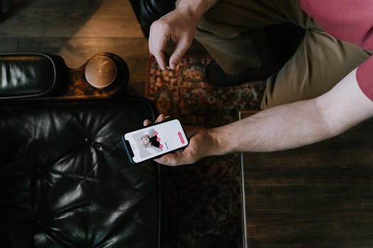 A person holding a smartphone with a dating app displayed while sitting on a leather chair.