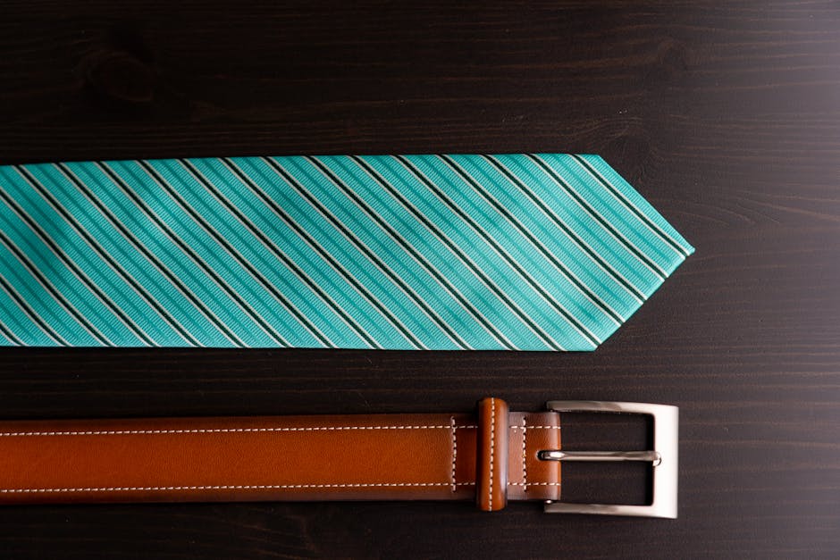 Stylish brown leather belt and turquoise striped necktie arranged on a dark wooden flat surface.