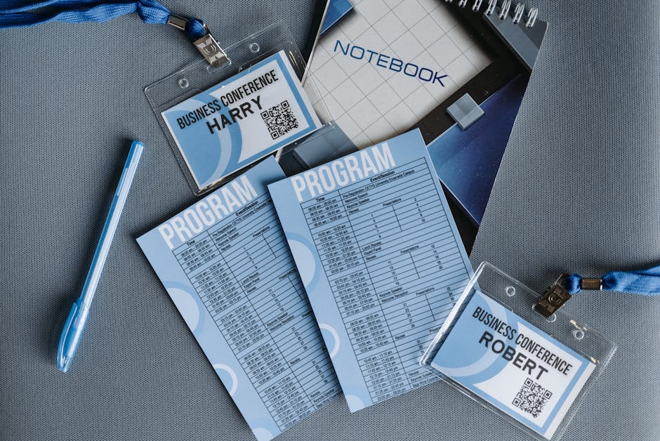 Flat lay of business conference materials including name tags, program, notebook, and pen.