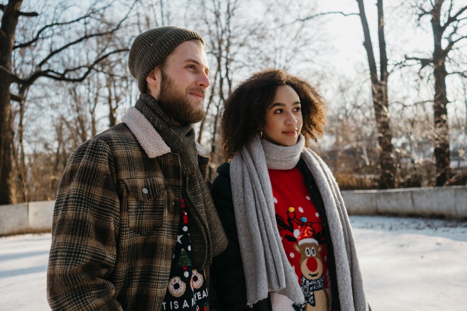 A smiling couple dressed in colorful winter clothes strolls outdoors on a snowy day.